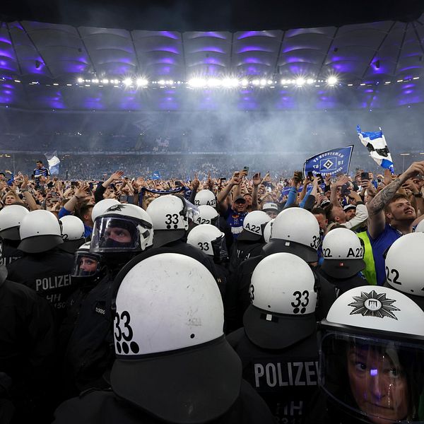 Poliser i hjälmar bildar kedja framför stor fotbollspublik på en upplyst arena.