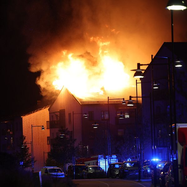 Stort hus i brand på natten, blåljus från räddningstjänst syns på gatan.