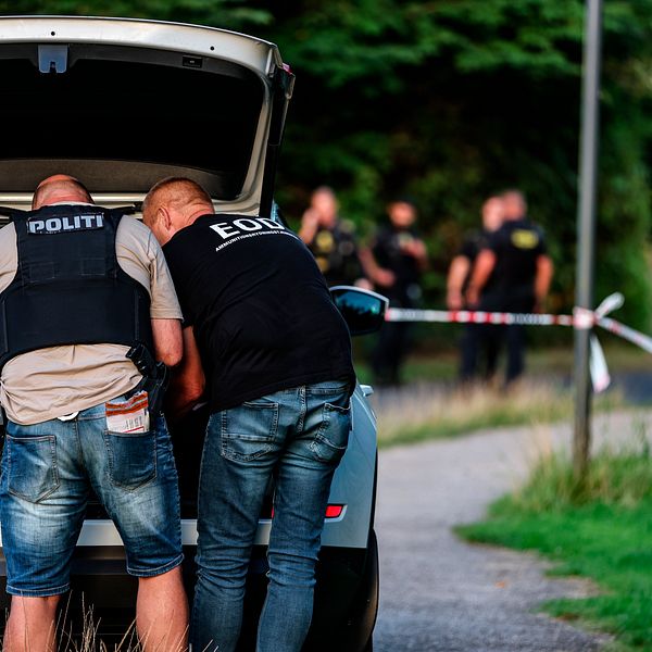 Två civilklädda poliser med skyddsväst står vid en bil.