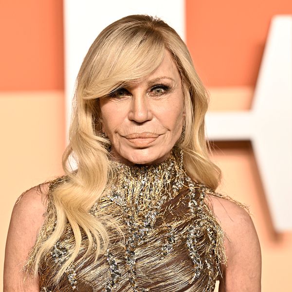 Donatella Versace med blont hår i glittrande klänning framför en orange bakgrund.