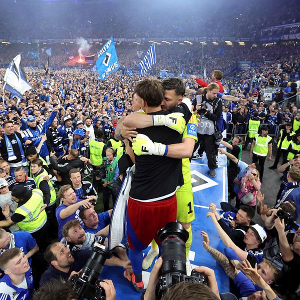 Fotbollsspelare firar med fans på en fullsatt arena efter en match, omgivna av vakter.