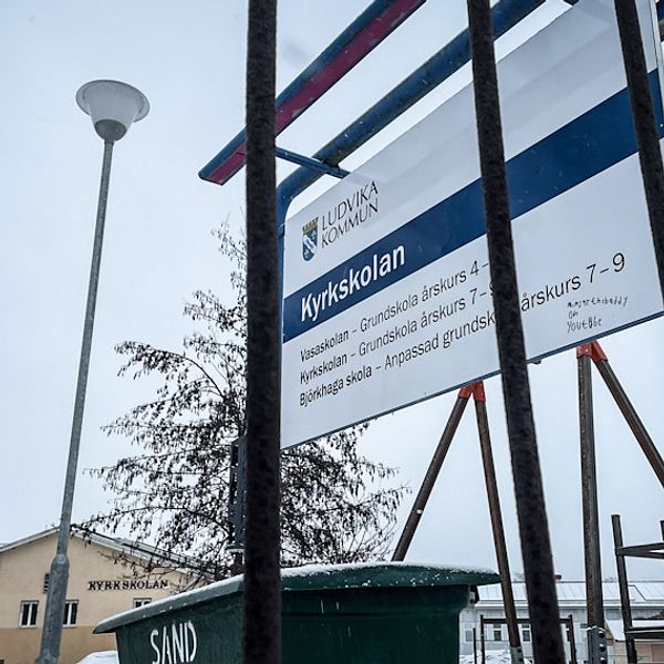 En informationsskylt utanför Kyrkskolan i Ludvika syns genom ett staket.