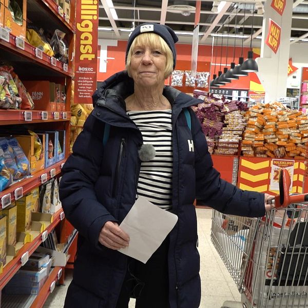 En kvinna står i en gång i en matvarubutik vid en kundvagn