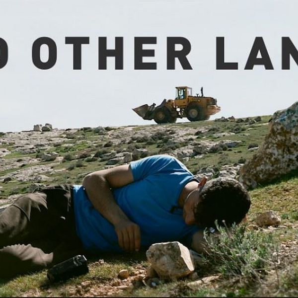 Man ligger på marken i ett kargt landskap. Texten ”No Other Land” syns.