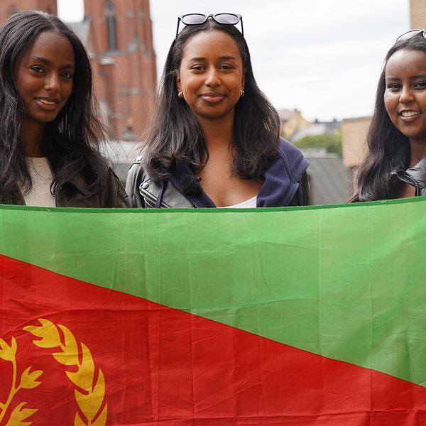 Tre unga tjejer håller Eritreas flagga