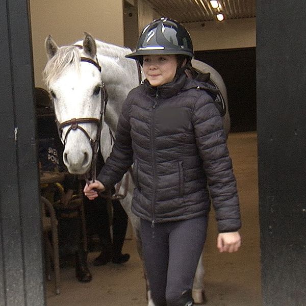 Ung ryttare leder en vit häst ut från ett stall. 12-åring ryttare tränar inför Gothenburg Horse Show.