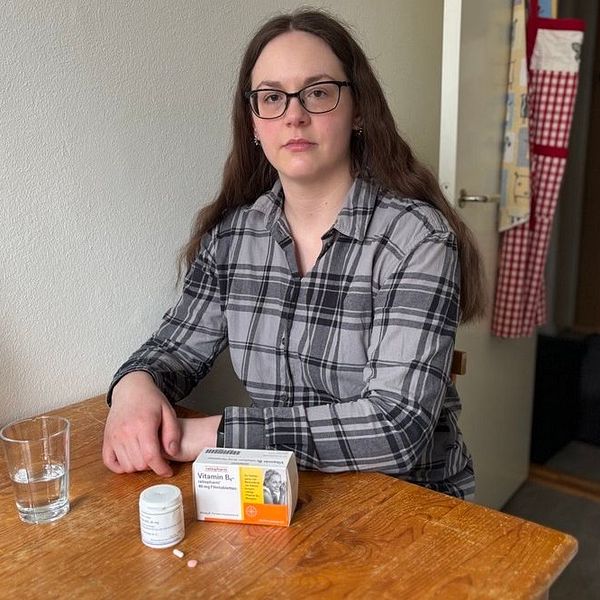 Elisabet sitter vid ett bord med läkemedel och ett glas vatten framför sig.