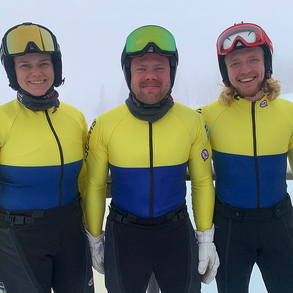 Tre personer i gul- och blåklädda tävlingsdräkter, representerande Sverige, står bredvid varandra i en dimmig utomhusmiljö. De bär hjälmar och handskar som tyder på att de deltar i en vintersport.