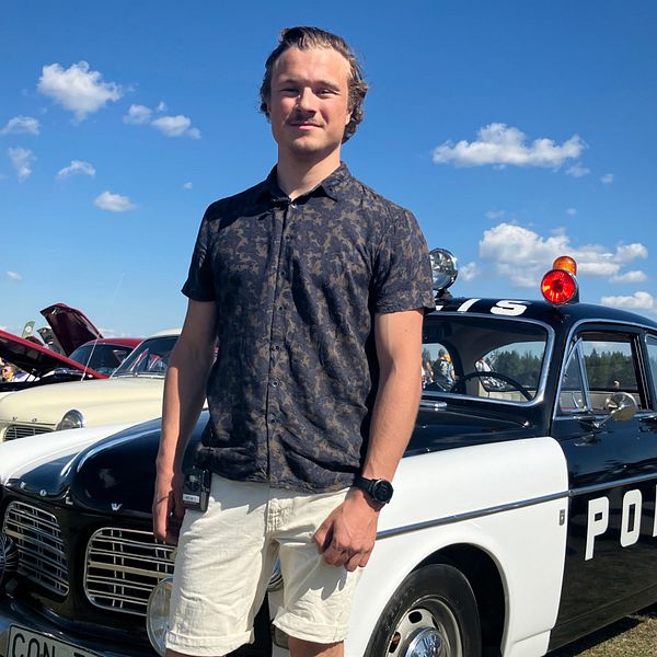 Arvid Jonsson, står i ett soligt Östersund framför en gammal polisbil från 68.