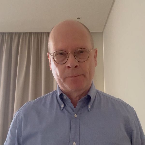 Mats Knutson står i ett rum med ljusa väggar och gardiner i bakgrunden.