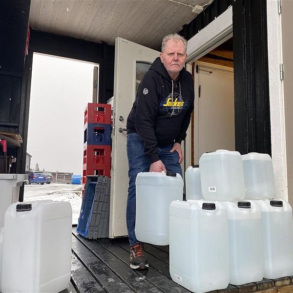 Man bär flera plastdunkar ut från en byggnad.
