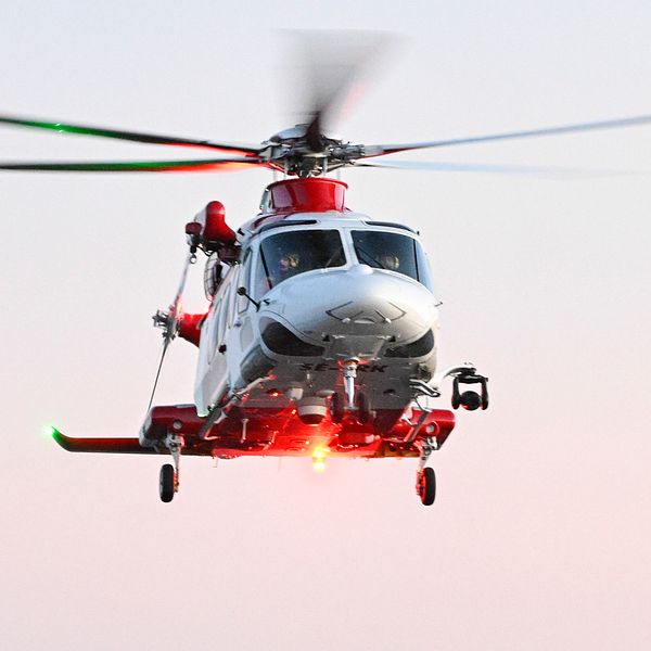 En räddningshelikopter flyger i luften under skymning med en person synlig vid sidan av helikoptern.