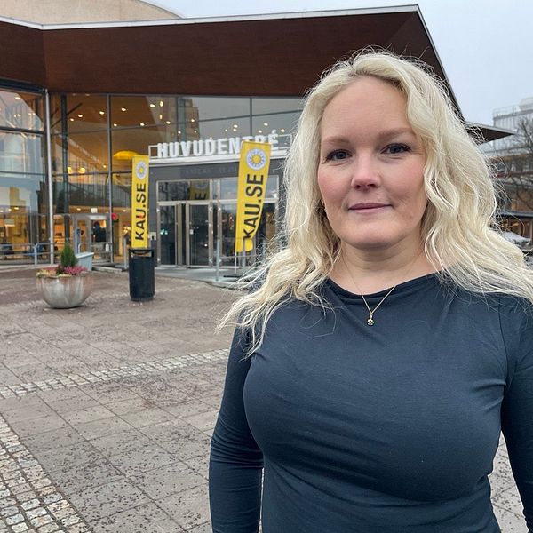 Anna Sjöberg står framför Karlstads universitet, Omgivningen är grå och regnig, med några planteringar och stenar på marken.