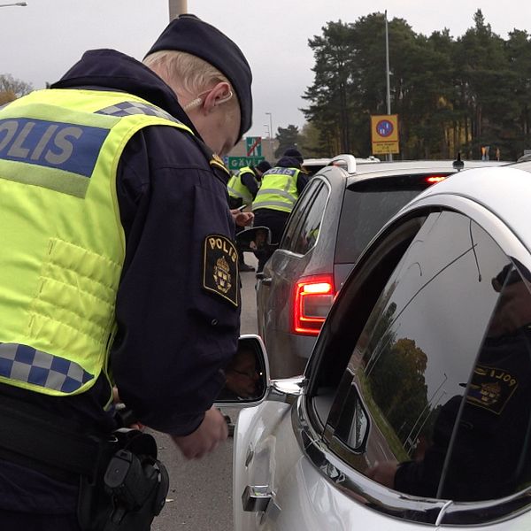 En polis i uniform genomför en trafikkontroll och pratar med en bilförare genom fönstret på en rad av bilar som står stilla på en landsväg.