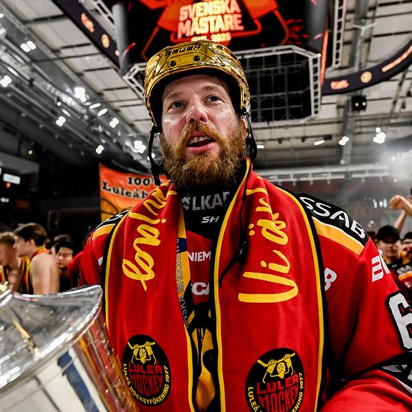 En hockeyspelare firar med pokal framför jublande supportrar i ishallen.