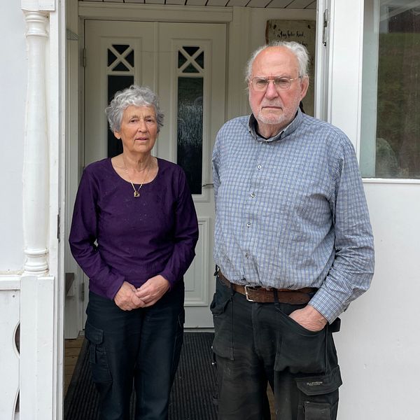 En kvinna och en man står utanför en vit verandadörr, kvinnan i lila tröja, mannen i blå skjorta.