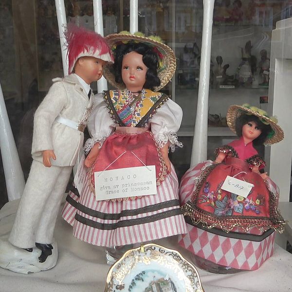 Tre dockor klädda i bationaldräkt uppställda i en monter. På ena dockan finns en skylt att den skänkts av Grace om Monaco