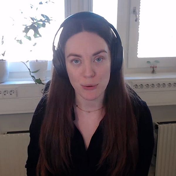 Person i svart tröja och hörlurar sitter framför ett vitt fönster med växter på fönsterbrädan.