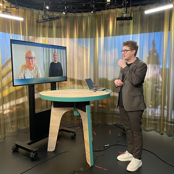 Magnus Bergevin står i en tv-studio. Zandra Ahkoila och en teckenspråkstolk syns på en skärm i ett videomöte.
