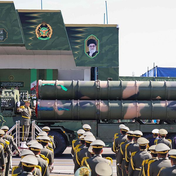Militärparad i Iran, med soldater och lastbil som bär missiler framför byggnad.