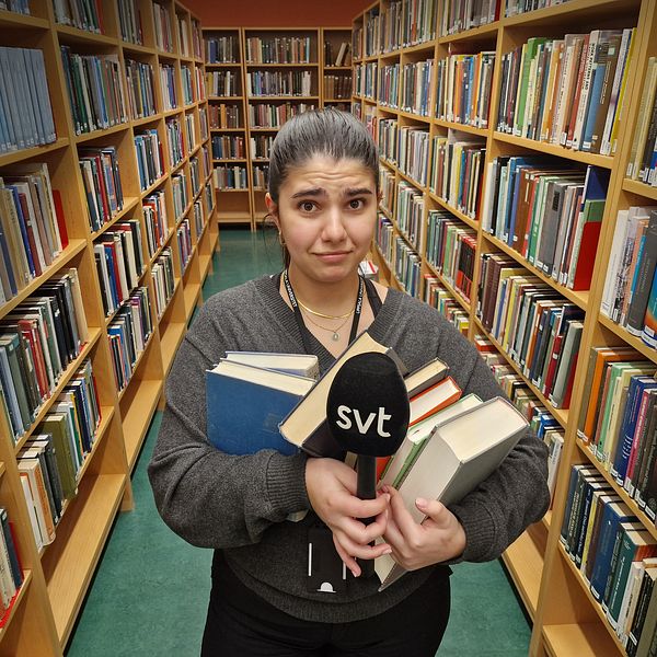 Person håller böcker och en SVT-mikrofon i en bibliotekskorridor.