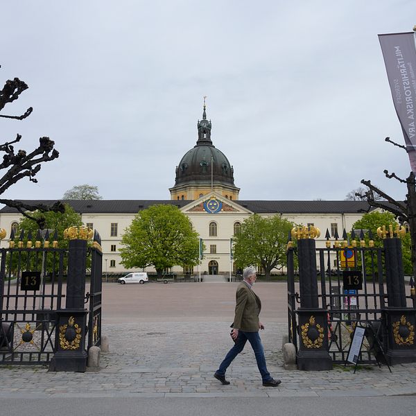 Slott med kupol bakom grindar, förbipasserande på gata i förgrunden