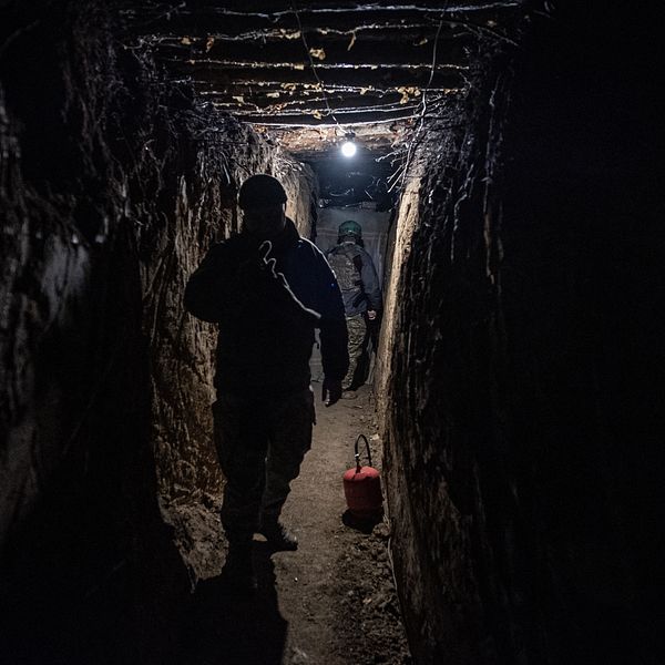Person går genom en mörk tunnel med svagt ljus i bakgrunden.