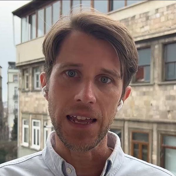 Gammaldags stenbyggnader i stadsmiljö, torn till vänster och träd i bakgrunden.