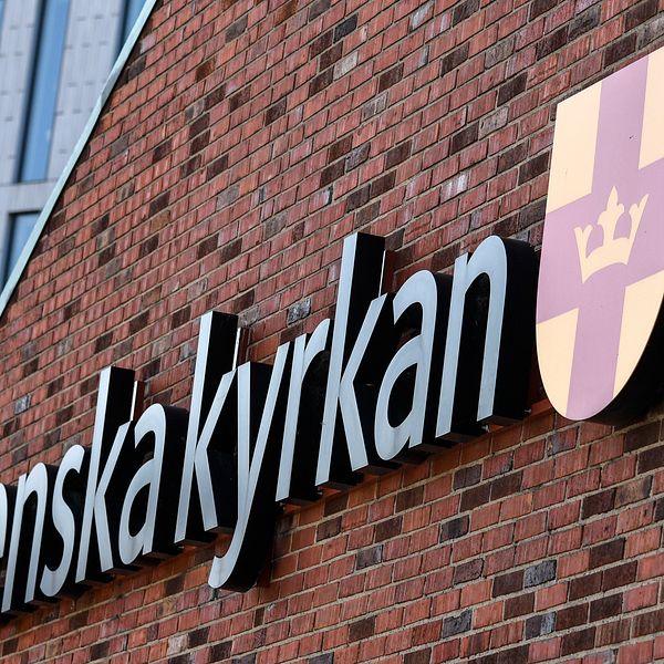 Svenska kyrkans logotyp och sköld på en tegelvägg.