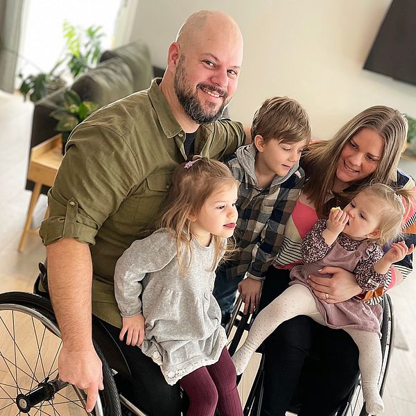 Stefan Olsson i rullstol tittar in i kameran, är omringad av sin familj