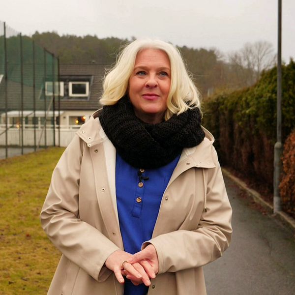 Cecilia Wendin i blont hår, beige kappa, blå tröja, jeans, går bland radhus i Göteborg.