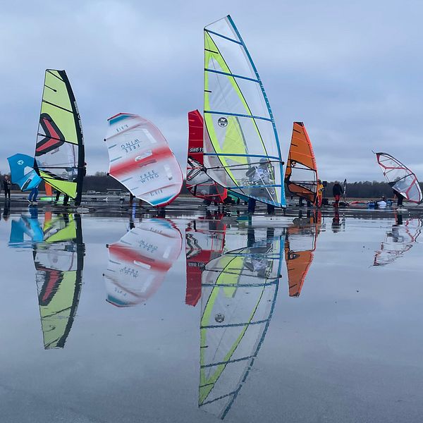Flera färgglada vindsurfingsegel står uppradade på Hjälmarens istäcke.