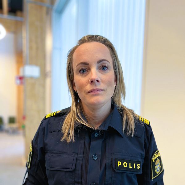 Svensk polis i uniform står inomhus med suddig bakgrund.