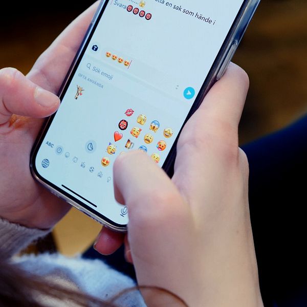 Ungdom håller en mobiltelefon med båda händerna och tittar på skärmen
