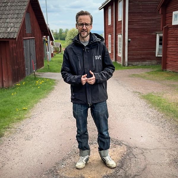 SVT:s reporter Henrik Kilefors står på en gårdsplan vid röda byggnader