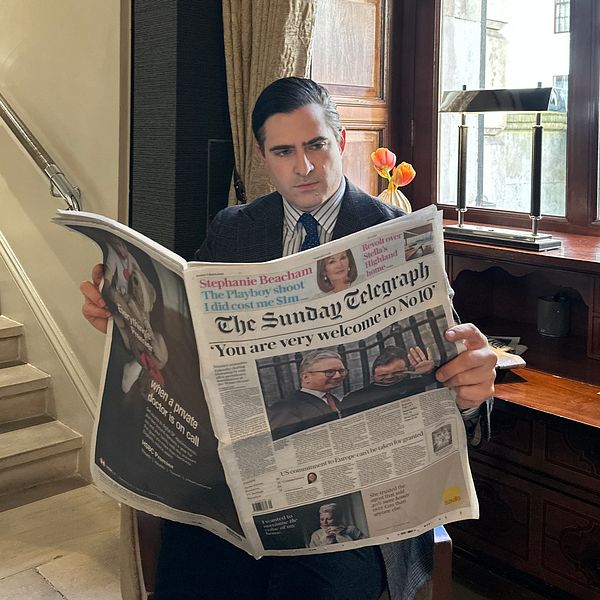 Person i kostym läser The Sunday Telegraph, står vid ett fönster nära en trappa.