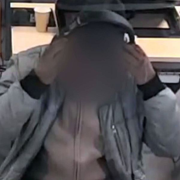 Person med suddat ansikte sitter vid dator och håller i hörlurar.