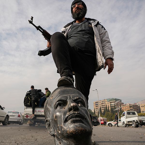 En beväpnad rebell står med ena foten på en skulptur föreställande av den avlidne presidenten Hafez Assad i Damaskus.