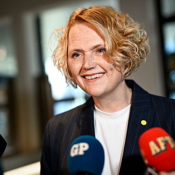Person intervjuas av flera journalister med mikrofoner från olika nyhetsmedier.