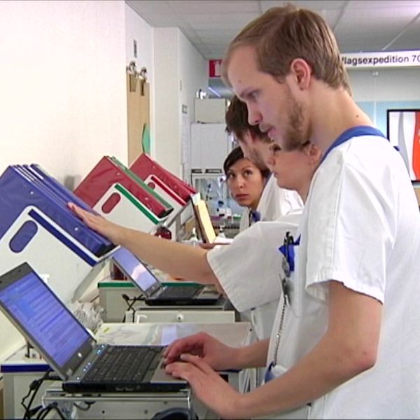Två vårdanställda arbetar vid datorer i en sjukhuskorridor medan de granskar patientdokumentation.