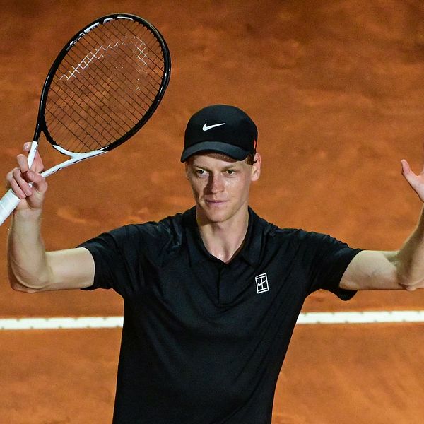 Tennisspelare i svart kläder lyfter armarna på en grusplan efter en poäng.
