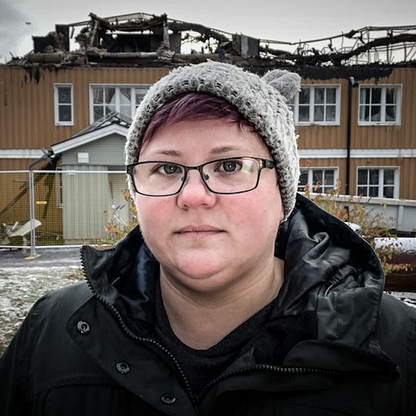 En ung kvinna står framför ett flerfamiljshuset som har brunnit.
