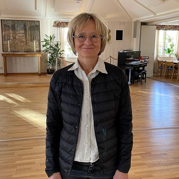 Kvinna med blont hår och glasögon ler mot kameran.