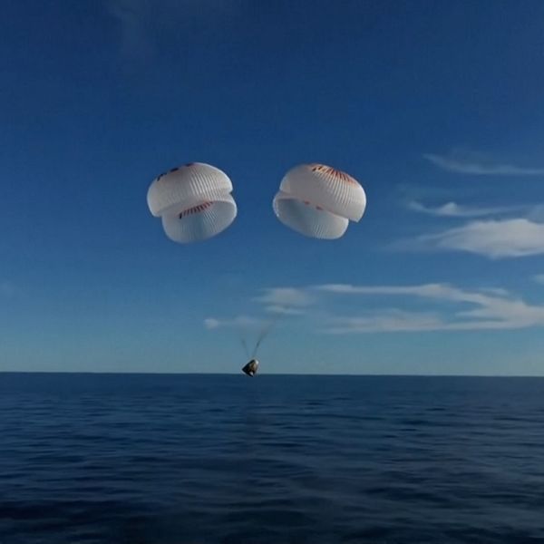 Två fallskärmar över havet med blå himmel och en farkost i vattnet.