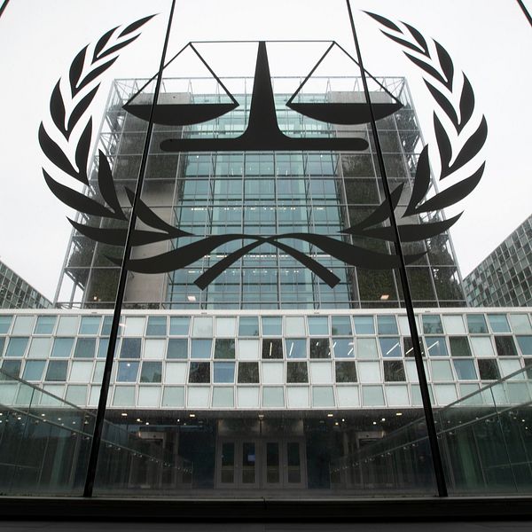 Fasaden av Internationella brottmålsdomstolens byggnad i Haag, med en stor logotyp med vågskål och olivkvistar synlig på glaset.