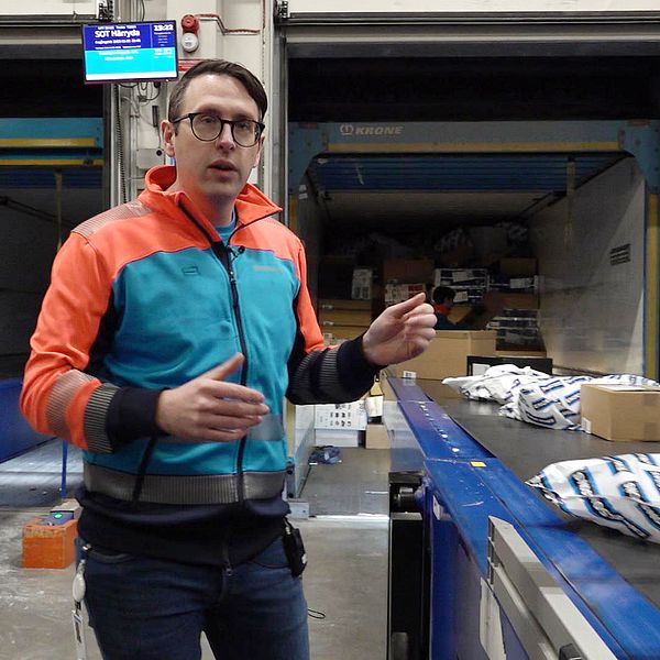 En man med glasögon står vid ett rullband med paket på postterminalen i Växjö.