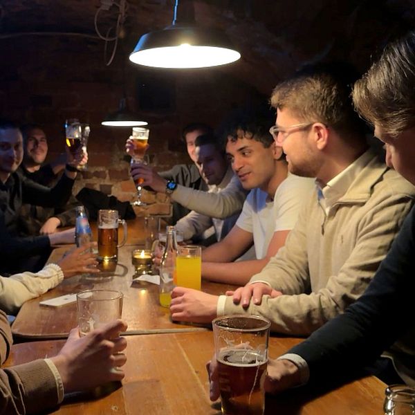 Ett större sällskap skålar och umgås runt ett långbord på en mörk pub.
