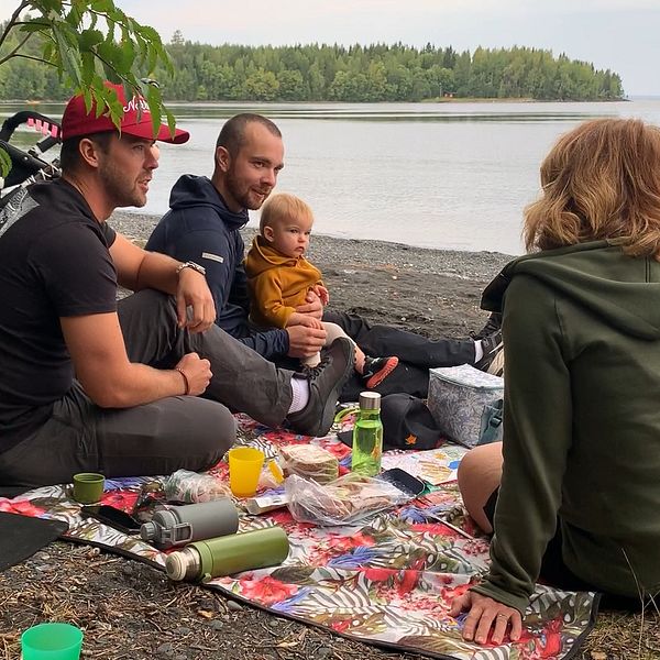 Familj sitter och fikar i skogen vid sjön