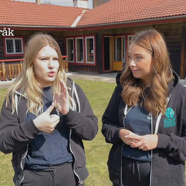 Julia Grahn och Mindie Norrie har på sig svarta kläder och står bredvid varandra på en gräsmatta utanför en skola.