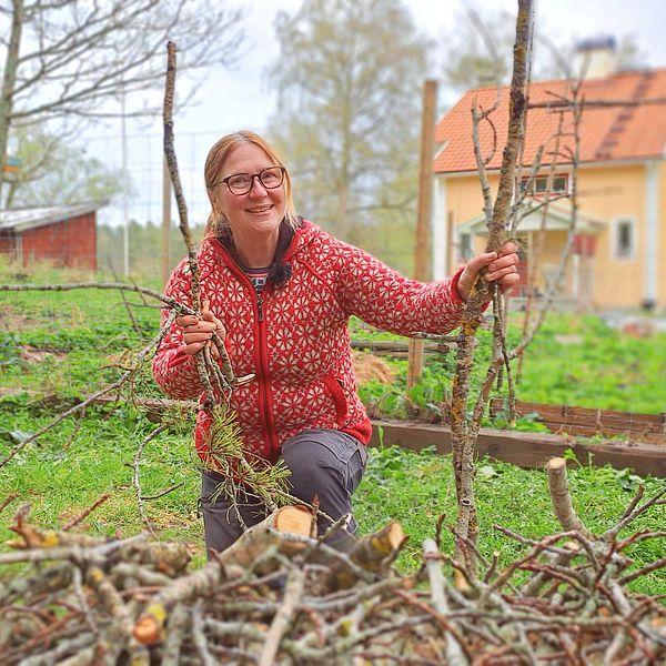 Hanna Pohjola står med kvistar och grenar i hand bakom en rishög framför sitt hus.